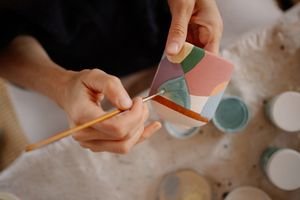 Close-up of hand painting a colorful ceramic pot with brush and pastel colors.