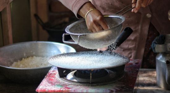 Woman preparing traditional rice dish over a gas stove in rustic setting, showcasing cultural cooking methods.